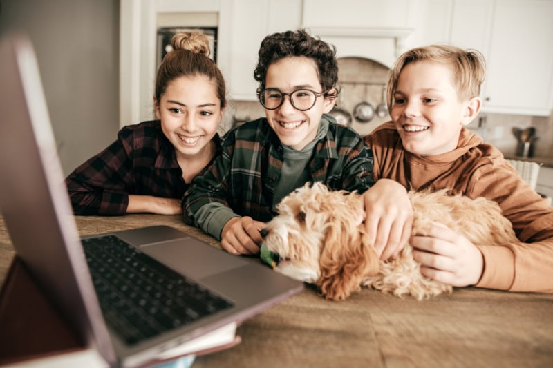 3 Reasons to Consider a Geothermal Heat Pump. Photo of three teenagers and their dog looking at a laptop in their kitchen.